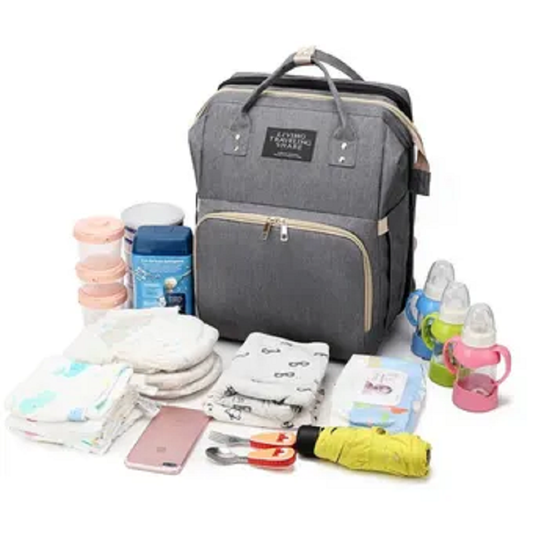 Pañalera gris tipo morral junto a pañales, teteros, ropa y accesorios para bebé.