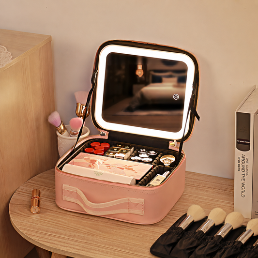 Cosmetiquera rosada abierta con espejo LED, maquillaje organizado y brochas sobre un tocador.
